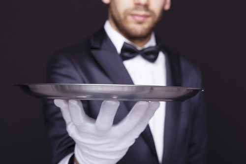 Close-up of a waiter holding an empty silver tray against dark b